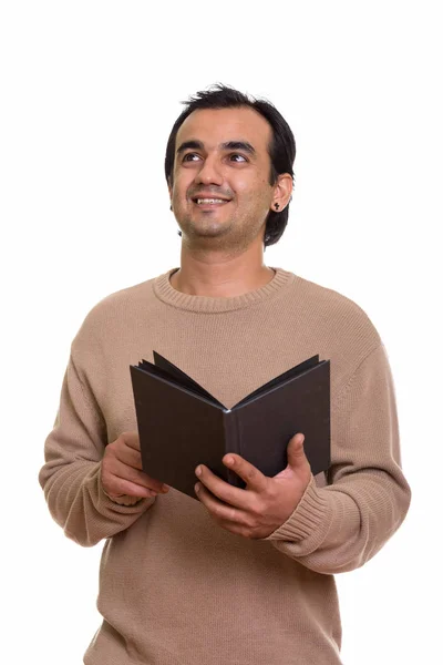 Studio shot of happy Persian man smiling while holding book and — Stock Photo, Image