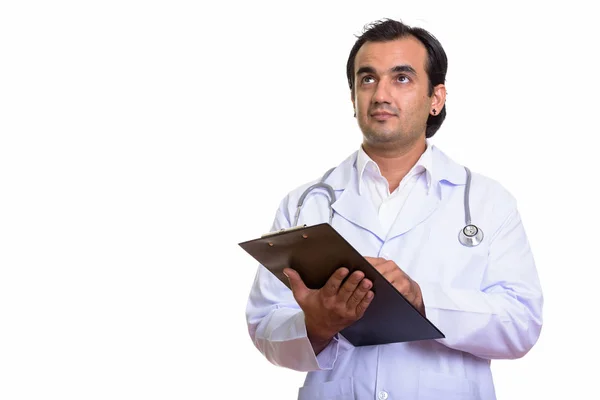 Studio shot of Persian man doctor holding clipboard while thinki — Stock Photo, Image