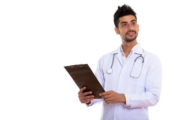 Studio shot of young Persian man doctor holding clipboard while — Stock Photo, Image