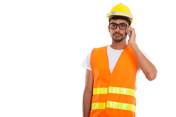 Studio shot of young Persian man construction worker talking on — Stock Photo, Image