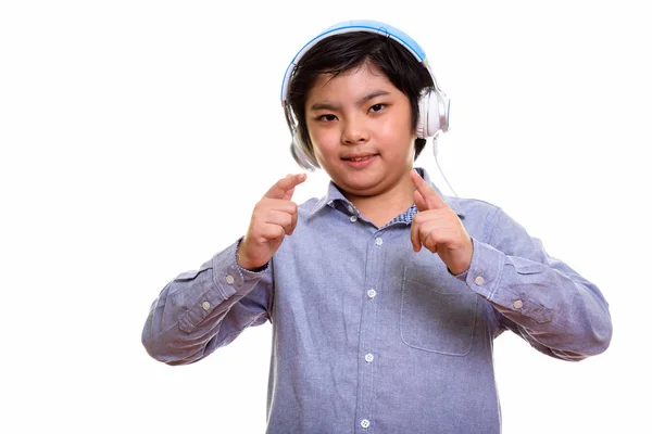 Studio shot of cute Japanese boy listening to music and pointing — Stock Photo, Image