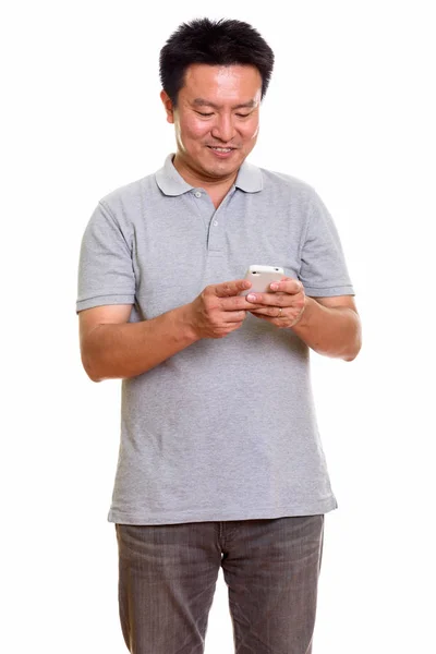 Studio shot of happy Japanese man smiling while using mobile pho — Stock Photo, Image