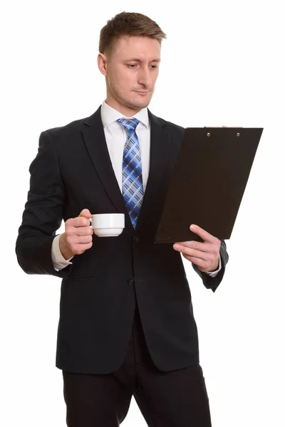 Komea valkoihoinen liikemies lukemassa leikepöytää juodessaan — kuvapankkivalokuva