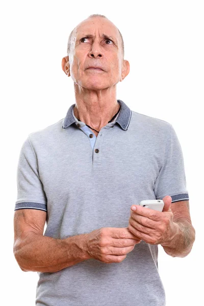 Studio shot van senior man met mobiele telefoon tijdens het denken — Stockfoto