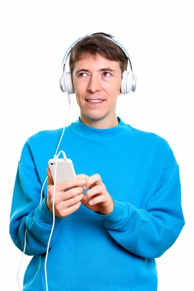 Ajattelevainen onnellinen mies hymyilee kuunnellen musiikkia ja käyttäen — kuvapankkivalokuva