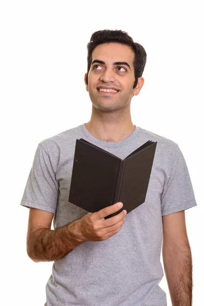 Jovem homem persa feliz segurando livro enquanto pensa — Fotografia de Stock