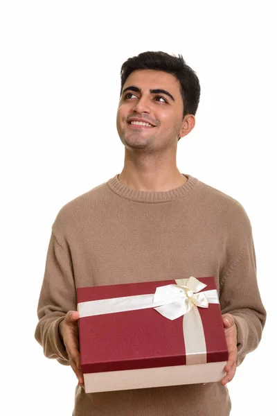 Young happy Persian man holding gift box while thinking ready fo — Stock Photo, Image