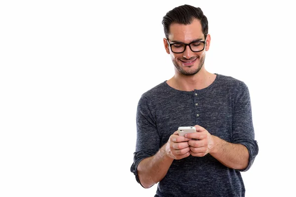 Studio shot of happy young handsome man smiling and using mobile — Stock Photo, Image