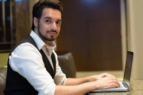 Young handsome Indian man using laptop in the lobby of hotel — Stock Photo, Image