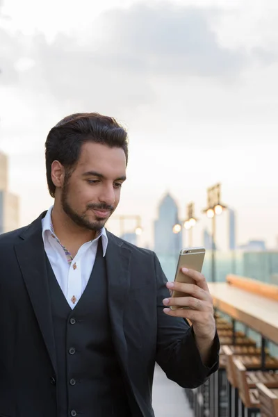 Young handsome Indian businessman using mobile phone at rooftop — Stock Photo, Image
