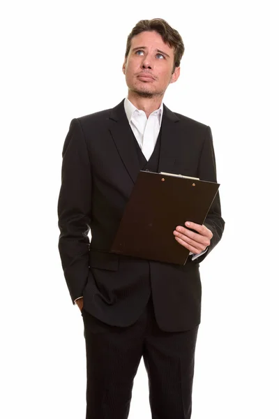 Handsome Caucasian businessman thinking while holding clipboard — Stock Photo, Image