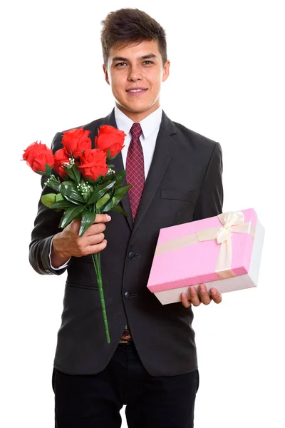 Nuori onnellinen liikemies hymyilee pitäen punaisia ruusuja ja lahjaa — kuvapankkivalokuva