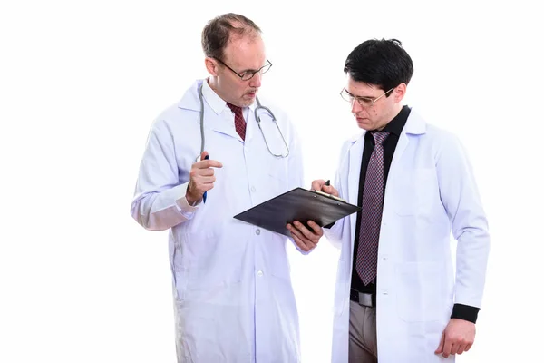 Mature man doctor and young man doctor both writing on clipboard — Stock Photo, Image