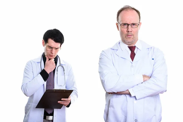 Mature homme médecin avec les bras croisés et jeune homme médecin lecture — Photo