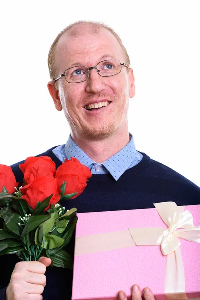 Удумливий щасливий чоловік посміхається, тримаючи червоні троянди і подарунковий бо — стокове фото