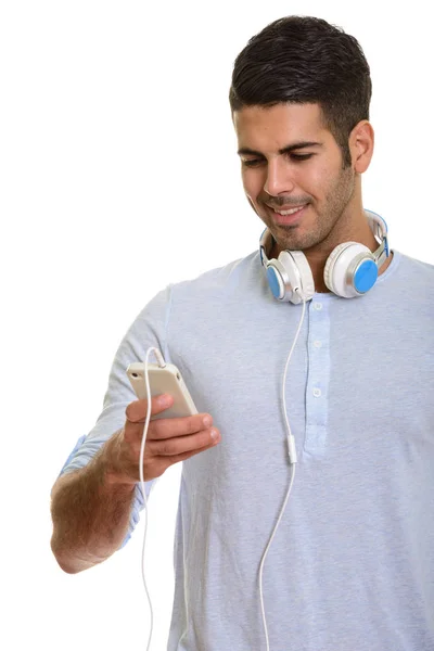 Joven hombre persa feliz sonriendo y usando el teléfono móvil mientras wea —  Fotos de Stock