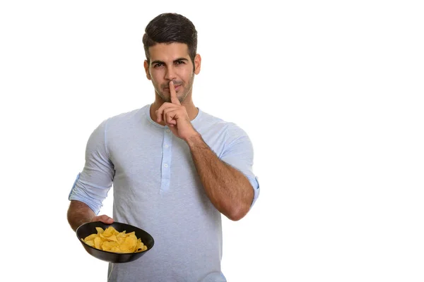 Young handsome Persian man holding bowl of potato chips with fin Stock Picture
