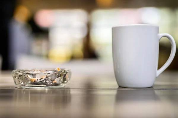 Cangkir kopi dan asbak dengan rokok di atas meja kayu di restau — Stok Foto