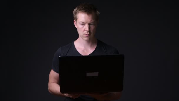 Jovem homem bonito com laptop contra fundo preto — Vídeo de Stock