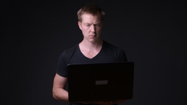 Jovem homem bonito com laptop contra fundo preto — Vídeo de Stock