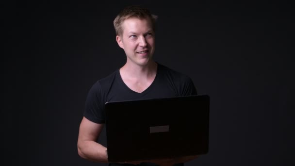 Young handsome man with laptop against black background — Stock Video