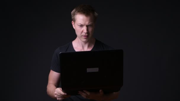 Молодий красивий чоловік з ноутбуком на чорному тлі — стокове відео