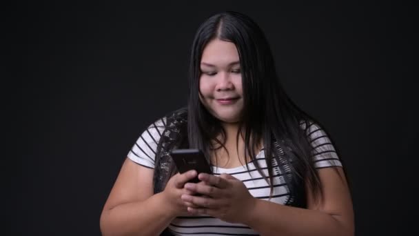 Vackra överviktiga asiatisk kvinna med mobiltelefon mot svart bakgrund — Stockvideo