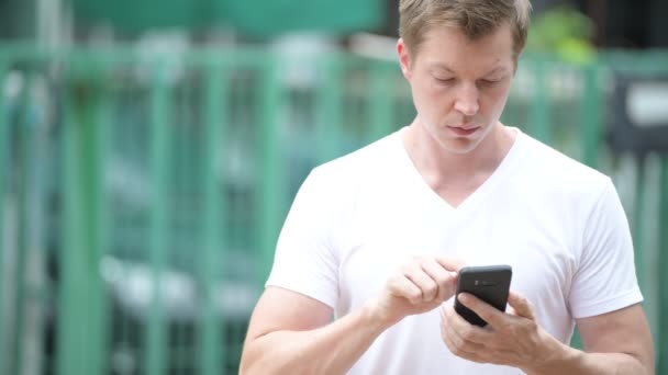 Fiatal jóképű férfi használ mozgatható telefon-az utcán szabadban — Stock videók
