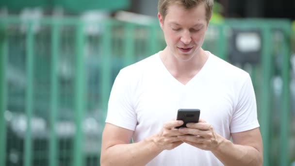 Joven hombre guapo usando el teléfono móvil en las calles al aire libre — Vídeo de stock