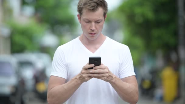 Joven hombre guapo usando el teléfono móvil en las calles al aire libre — Vídeos de Stock