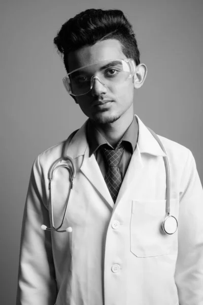Молодой индийский врач в защитных очках на сером фоне — стоковое фото
