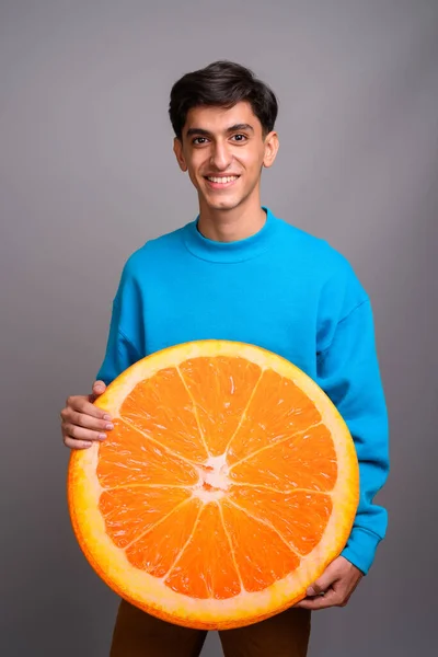 Giovane ragazzo adolescente persiano che tiene una grande fetta di frutta arancione — Foto Stock