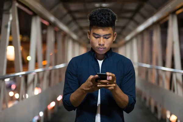 Νεαρός Ασιάτης που χρησιμοποιεί το τηλέφωνο στη γέφυρα το βράδυ — Φωτογραφία Αρχείου