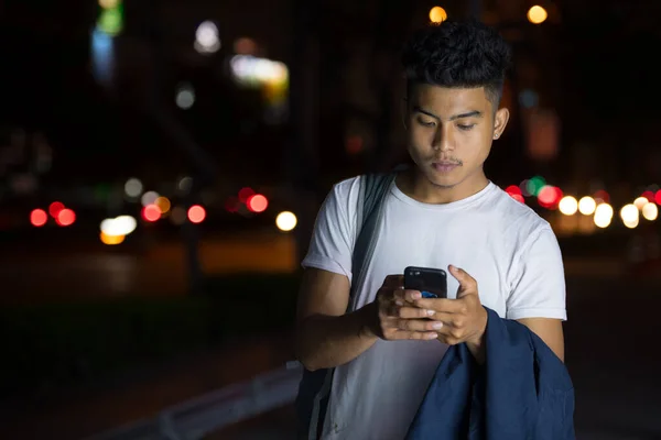 Νεαρός Ασιάτης που χρησιμοποιεί το τηλέφωνο στους δρόμους της πόλης τη νύχτα — Φωτογραφία Αρχείου