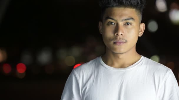 Visage de jeune homme asiatique heureux souriant dans les rues de la ville la nuit — Video