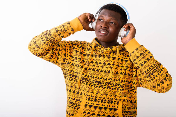 Studio shot of young happy black African man smiling while thinking and listening to music against white background