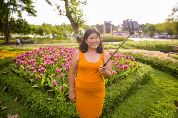 Asian woman taking selfie with mobile phone attach to selfie stick in park — Stock Photo, Image