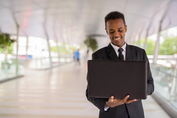 Gelukkig Afrikaans zakenman buiten met behulp van laptop computer terwijl glimlachen — Stockfoto