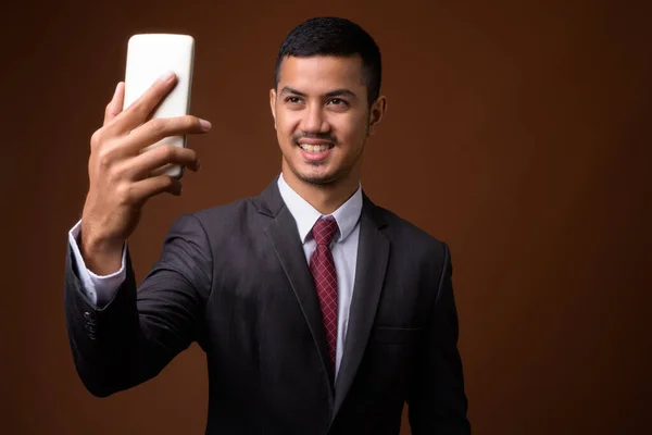 Молодой многонациональный азиатский бизнесмен на коричневом фоне — стоковое фото