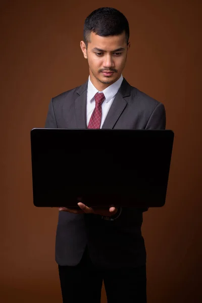 Young multi-ethnic Asian businessman against brown background — Stock Photo, Image