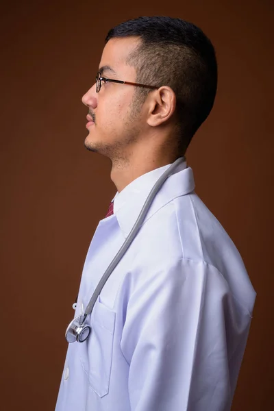 Młody człowiek Asian wieloetnicznego lekarz na brązowym tle — Zdjęcie stockowe