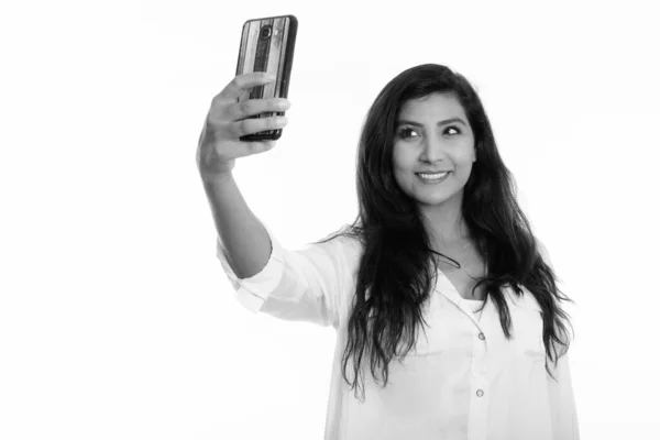 Studio shot of young happy Persian woman smiling while taking selfie picture with mobile phone — ストック写真