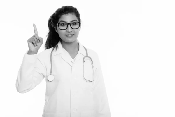Estudio disparo de joven feliz médico mujer persa sonriendo mientras señala con el dedo hacia arriba — Foto de Stock