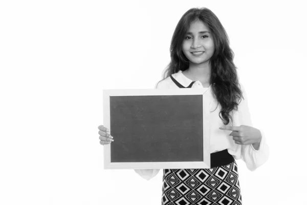 Studio shot of young happy Persian businesswoman smiling while holding and pointing at blank blackboard — ストック写真