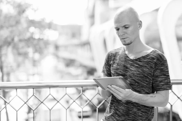 Young handsome bald man using digital tablet on the footbridge against view of the city streets — Stock Photo, Image