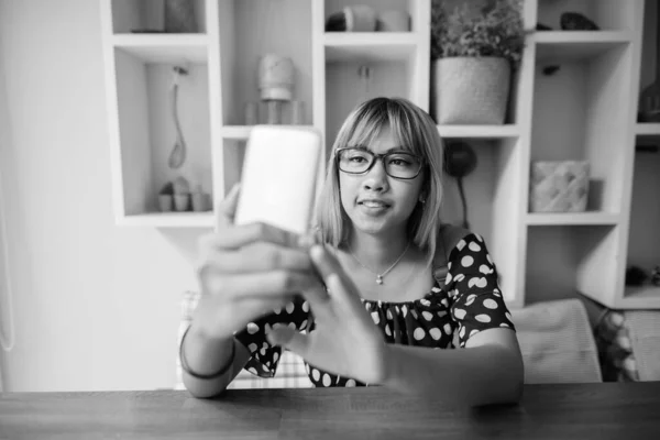 Young Asian teenage girl using phone at home in black and white — Stock Photo, Image