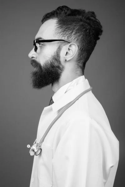 Молодой красивый бородатый персидский врач на сером фоне — стоковое фото