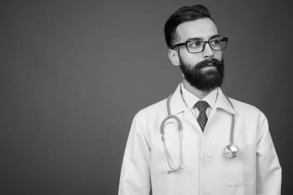 Молодой красивый бородатый персидский врач на сером фоне — стоковое фото