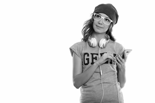 Estúdio tiro de geek menina segurando telefone celular ao pensar com fones de ouvido em torno do pescoço — Fotografia de Stock