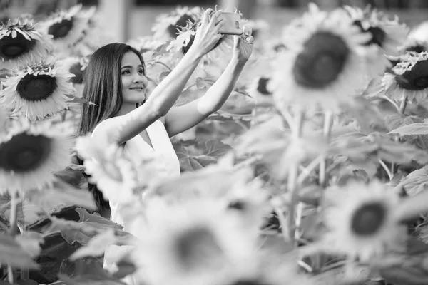 Jonge gelukkig Aziatische vrouw die lacht tijdens het nemen van selfie foto met mobiele telefoon op het gebied van bloeiende zonnebloemen — Stockfoto